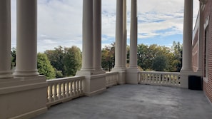 A balcony with white columns and a view of trees and a brick building.