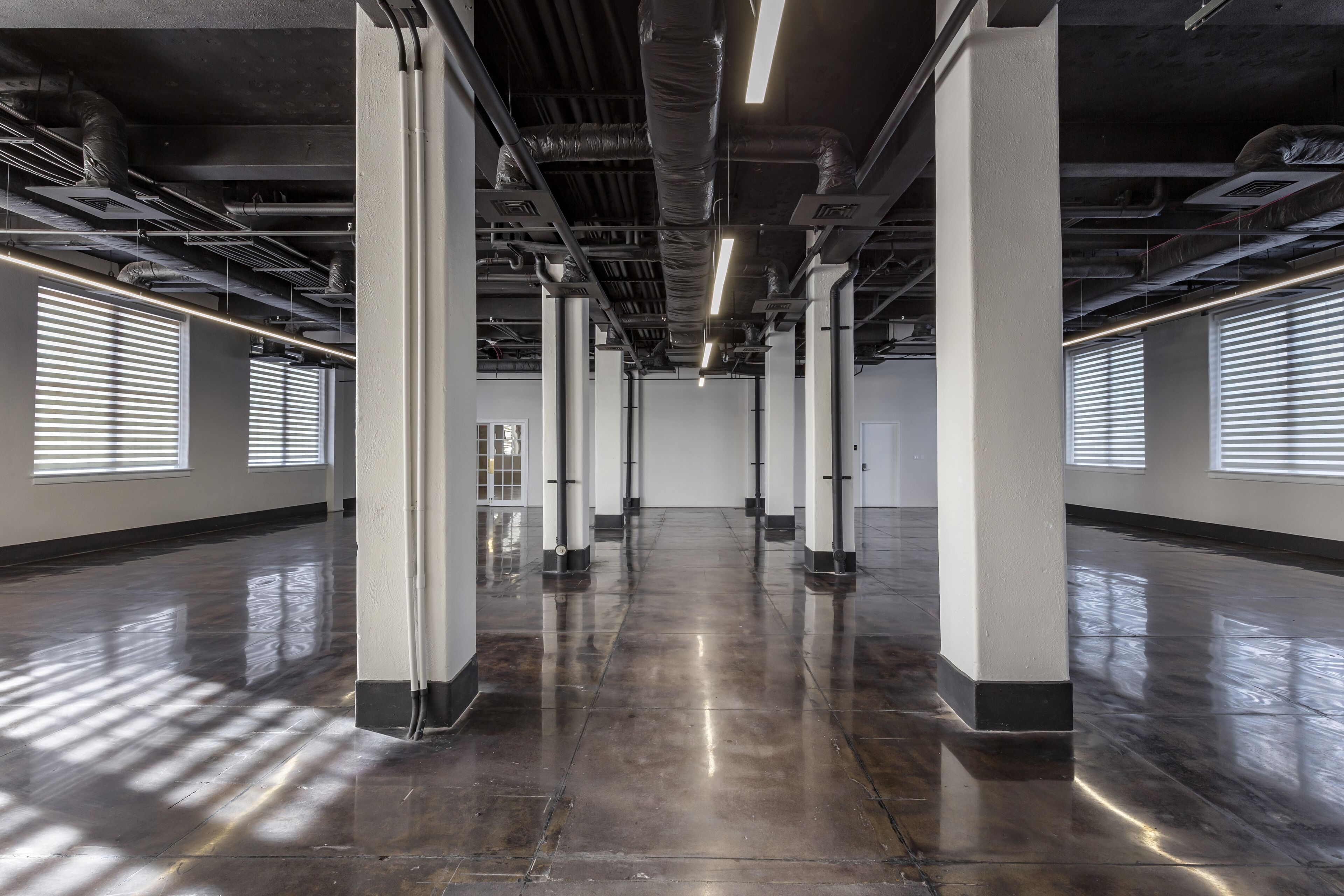 A spacious, industrial-style interior with high ceilings, exposed ductwork, and large windows with blinds.