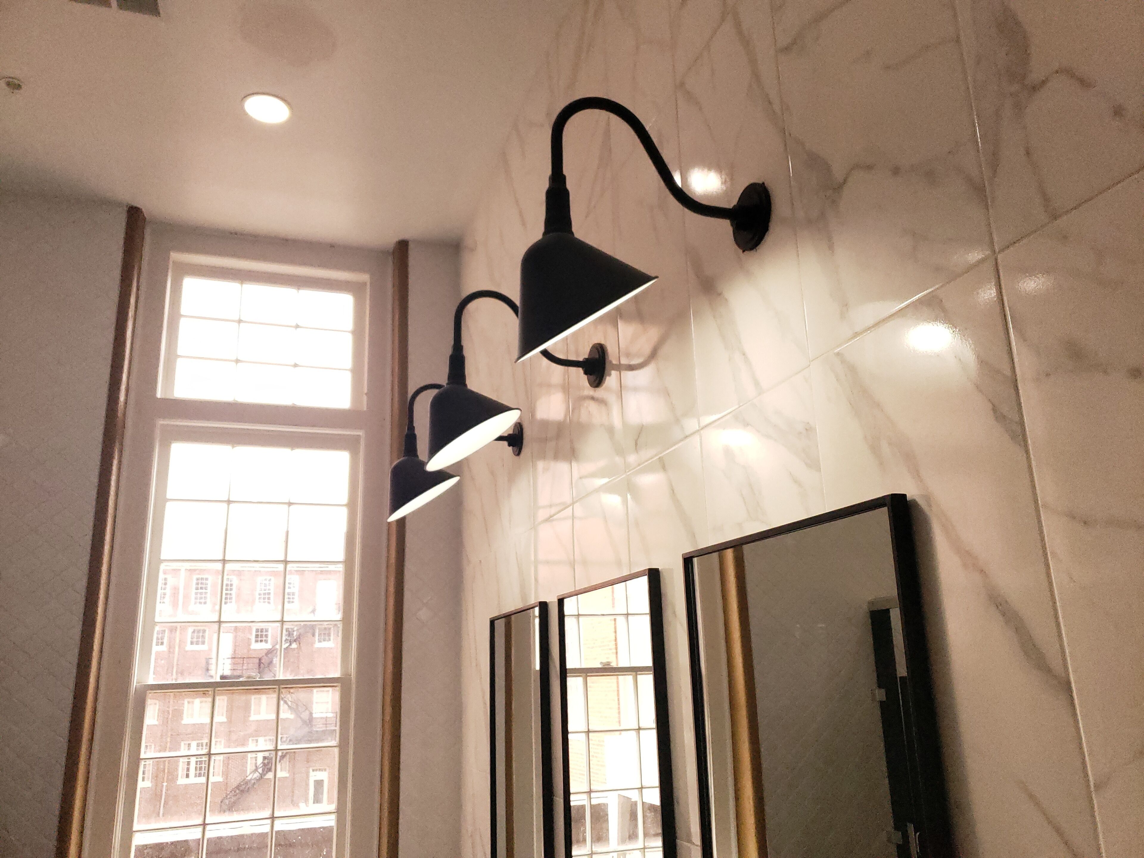 Een badkamer met een groot raam, een spiegel en twee wandlampen.
