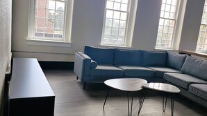 A modern living room with a blue sectional sofa, two round coffee tables, and large windows providing natural light.