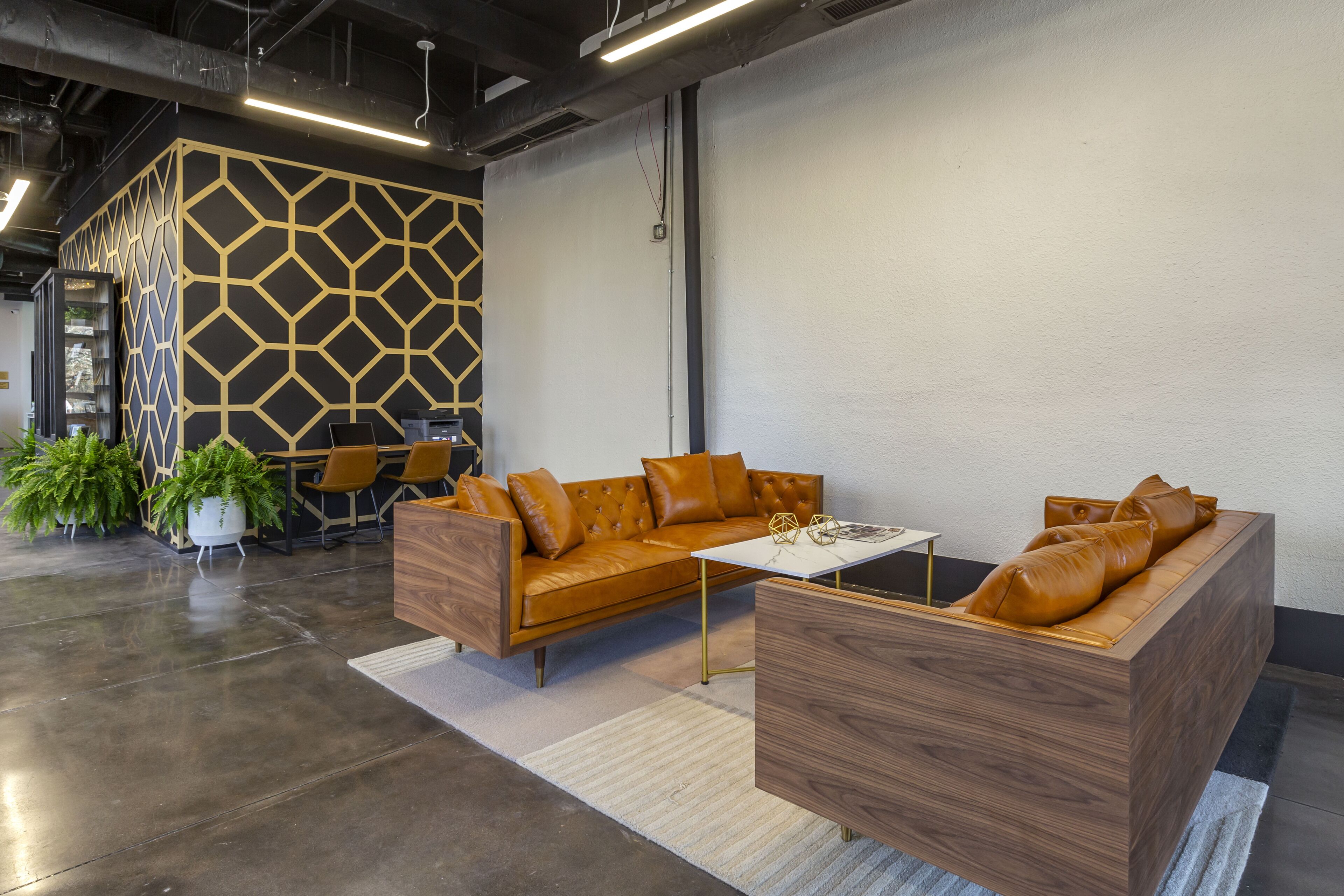 A modern office space with a sectional sofa, a coffee table, and a geometric patterned wall.