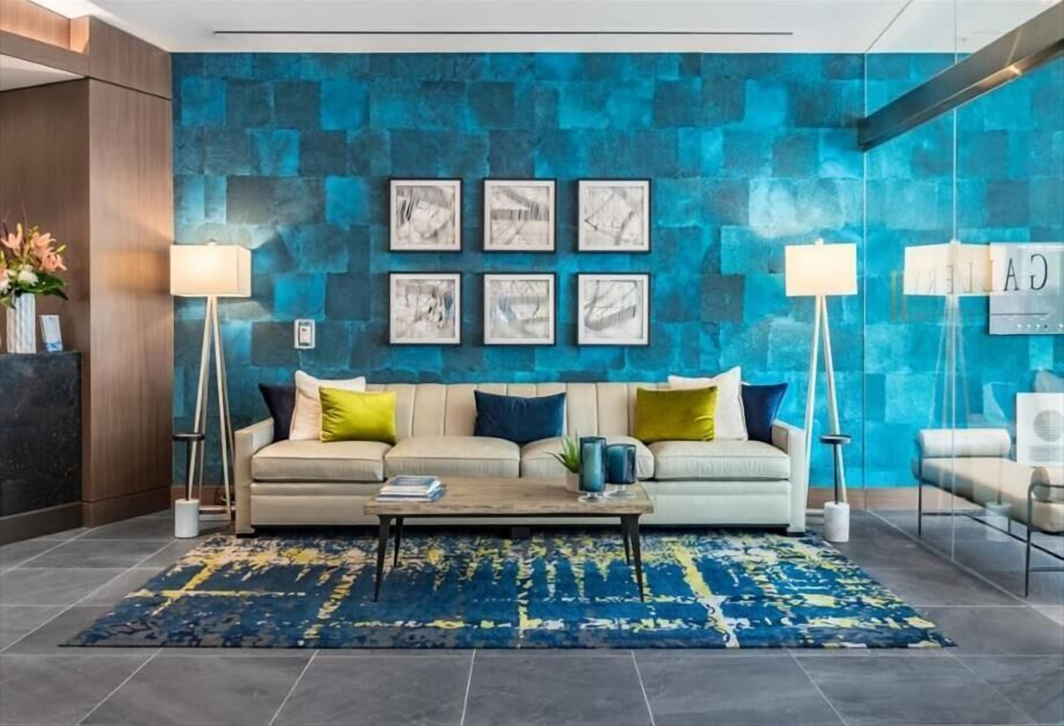 A modern lobby with a blue textured wall, a beige sofa with colorful cushions, a coffee table, and two floor lamps.