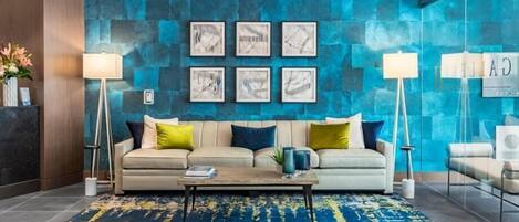 A modern lobby with a blue textured wall, a beige sofa with colorful cushions, a coffee table, and two floor lamps.