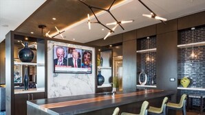 A modern kitchen with a marble island, bar stools, and a television displaying news.