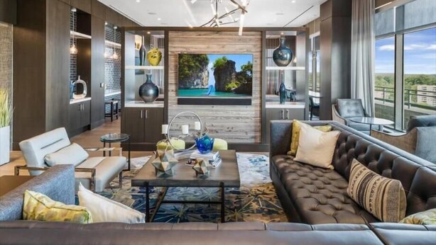 A modern living room with a large flat-screen TV, comfortable seating, and a view of the outdoors.