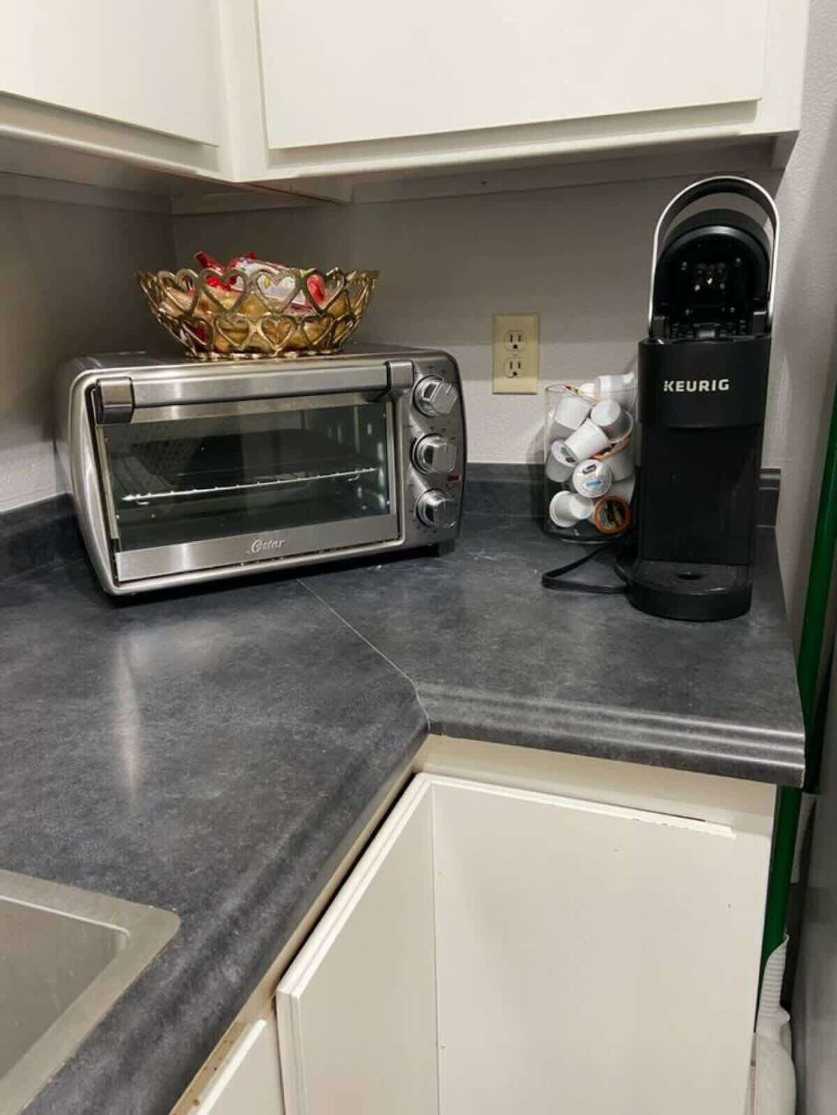 Una kitchenette con horno tostador, cafetera y un bol en la encimera.
