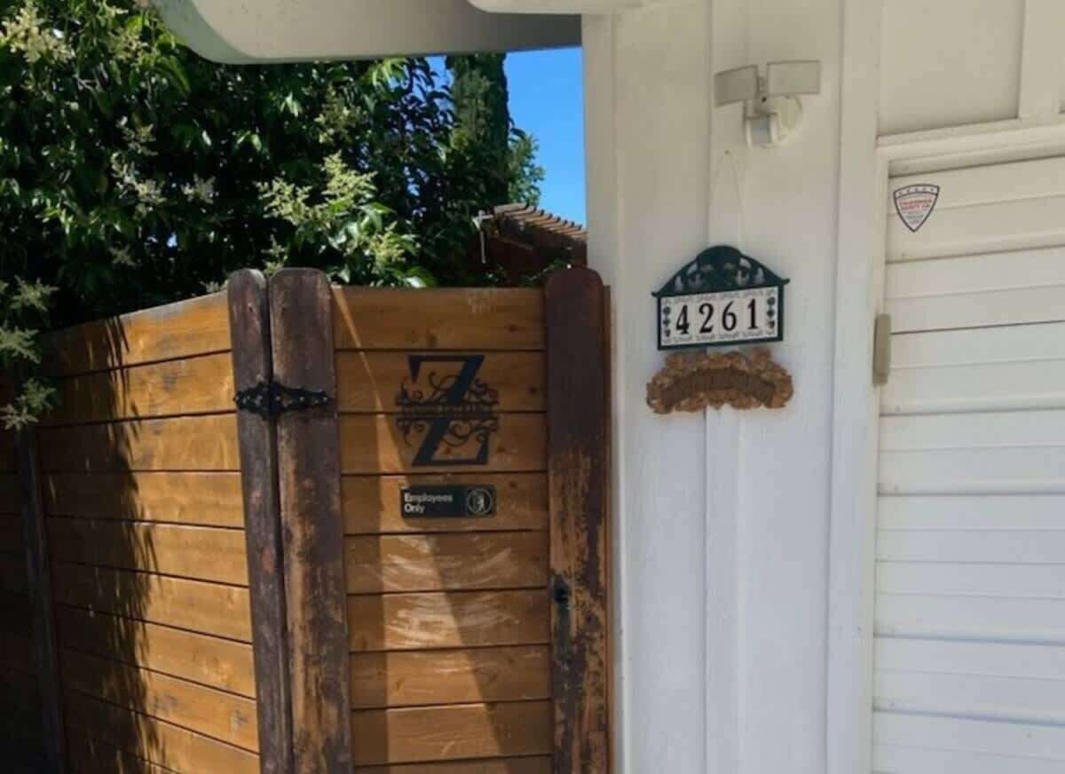 A wooden gate with a number plate, a white garage door, and a small sign above the door.