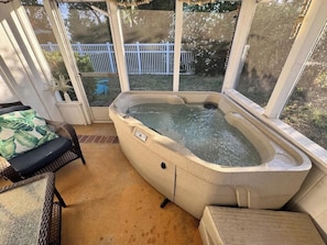 Un solárium con jacuzzi, mobiliario de mimbre y vistas a una cerca blanca y árboles.