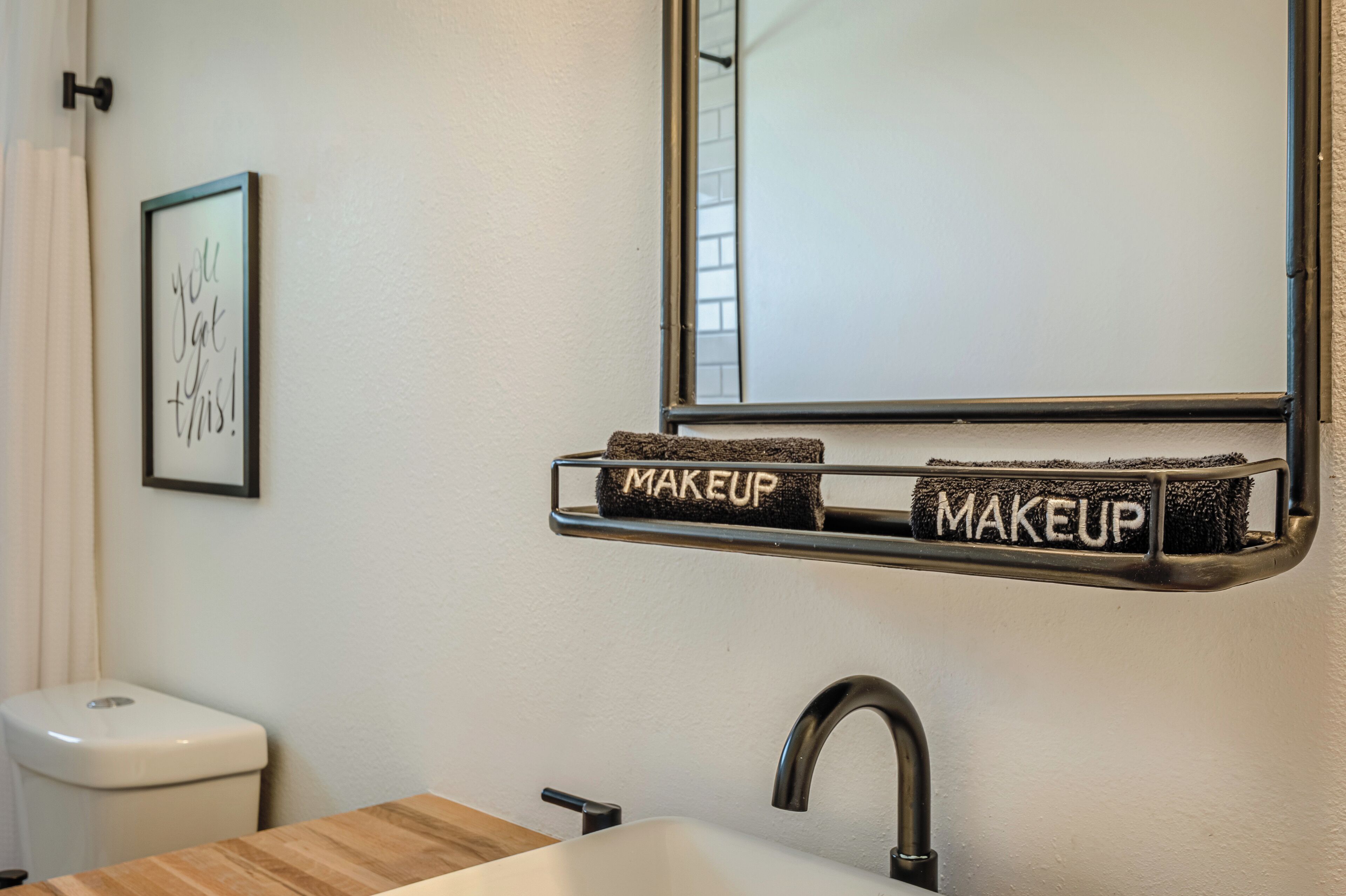 A bathroom with a sink, a mirror, and a towel rack with towels labeled "MAKEUP".