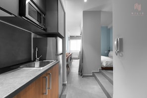 A modern kitchen with a microwave, sink, and wooden cabinets. A dining area with a table and chairs is visible in the background. - Big Apple 4 Nilie Hospitality MGMT (Thessaloniki)