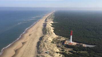 Vue aérienne d’une plage avec un phare et une zone boisée.