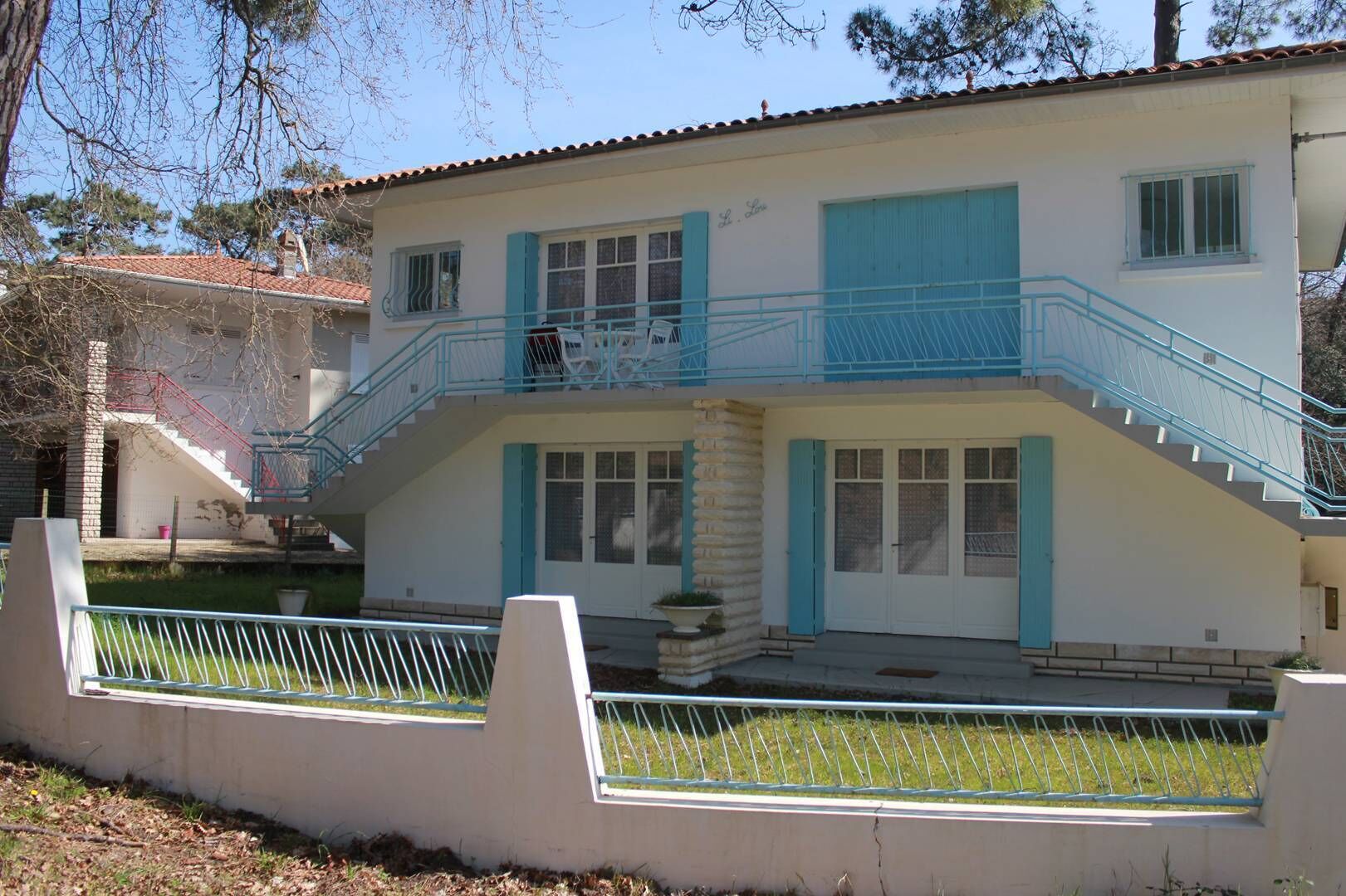 Un bâtiment à deux étages doté d’un balcon, d’un escalier et d’un petit jardin.