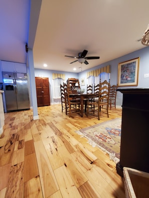 Uma sala de jantar com mesa e cadeiras de madeira, ventilador de teto e geladeira.