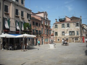 Une place publique dallée de pierres, dotée de sièges extérieurs et bordée de bâtiments historiques avec des balcons.