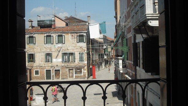 A balcony with a view of a narrow street lined with historic buildings, a clear sky, and a hanging light fixture. - Elegant and modern flat, historical centre wi-fi M0270422272 (Venezia)
