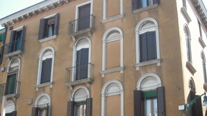 A multi-story building with a classic architectural style, featuring arched windows, shutters, and a balcony on the second floor. - Elegant and modern flat, historical centre wi-fi M0270422272 (Venezia)