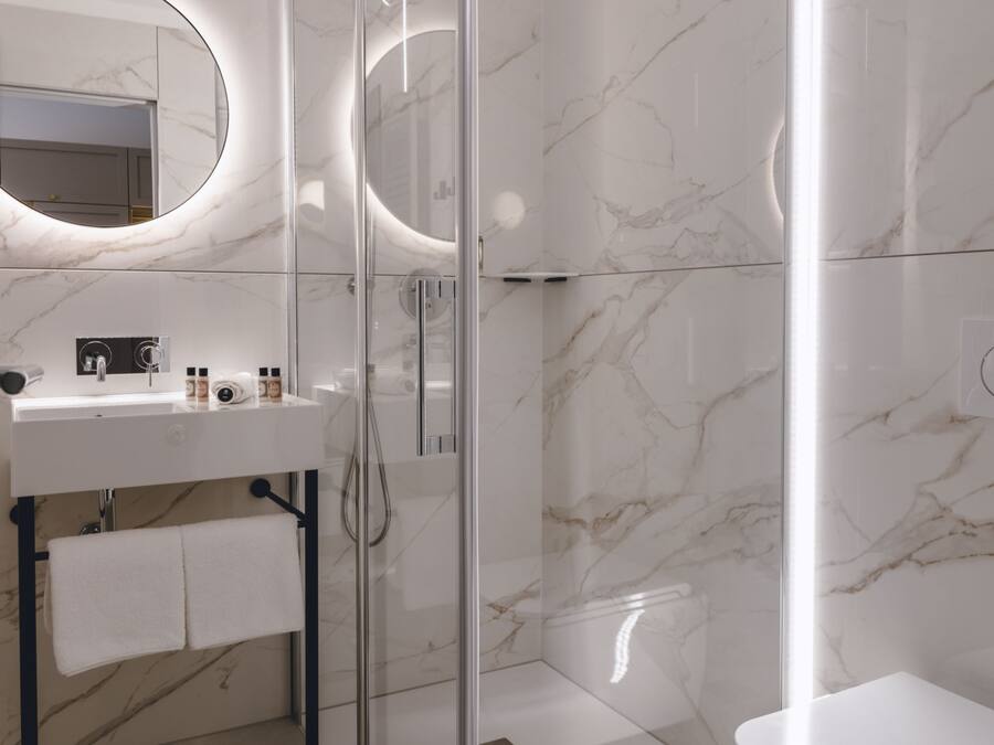 A modern bathroom with a glass-enclosed shower, a white sink with a mirror above it, and a toilet.