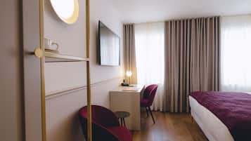 Habitación de hotel con cama, escritorio, silla, televisor y ventana con cortinas.