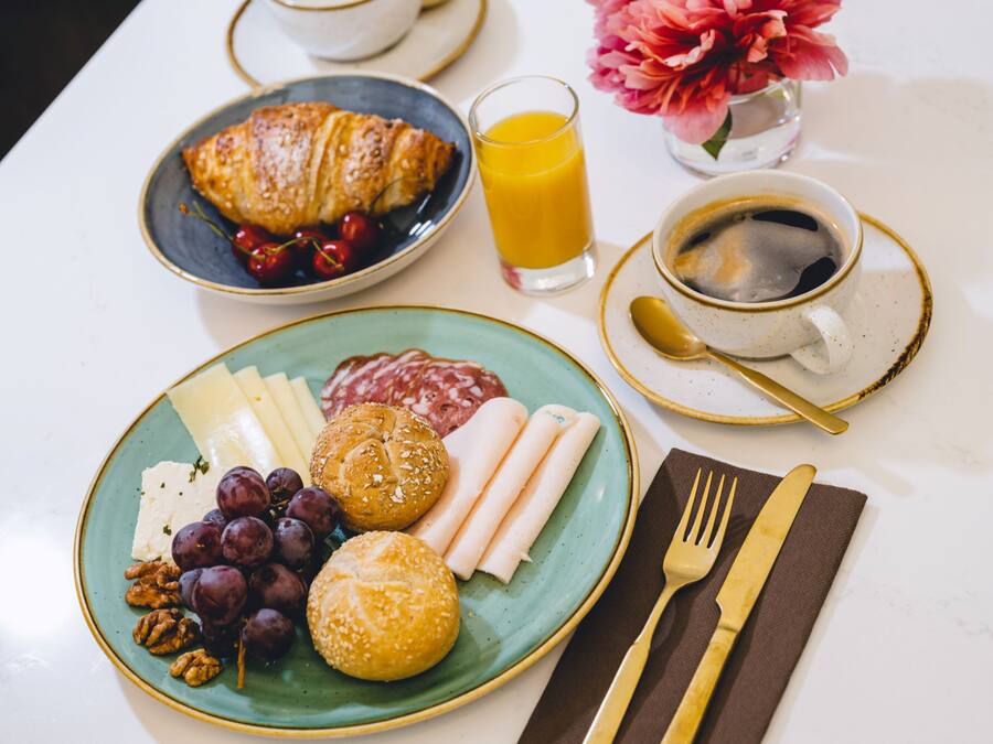 A breakfast setting with croissants, cheese, grapes, nuts, and a plate of meats.
