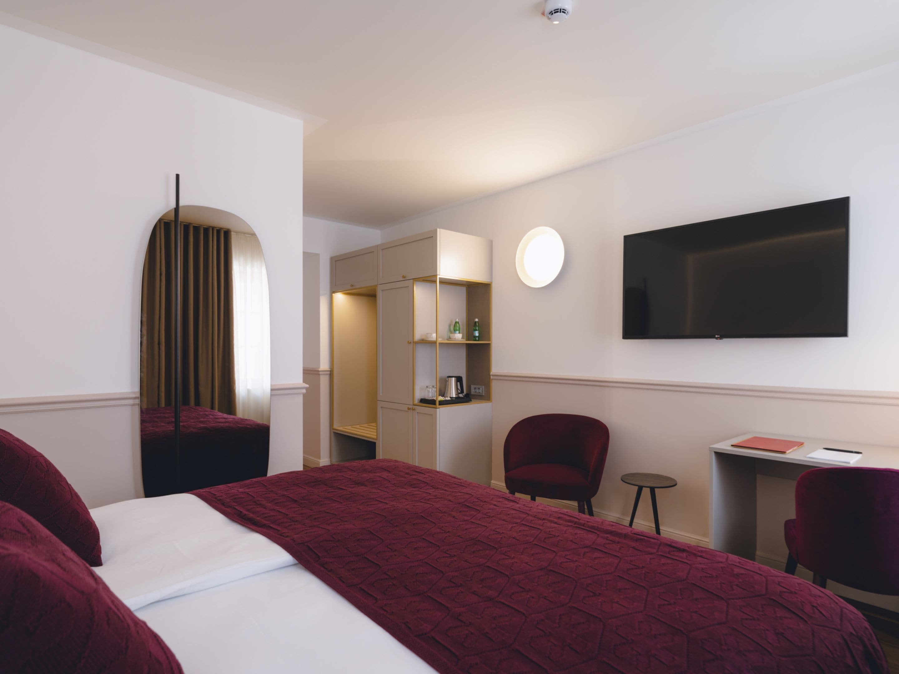 Ein Hotelzimmer mit einem großen Bett, einem an der Wand montierten Fernseher, einem Schreibtisch mit Stuhl und einem Spiegel.