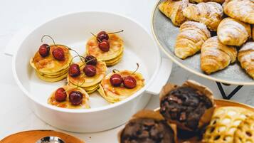 A variety of pastries including pancakes topped with cherries, croissants, and other baked goods.