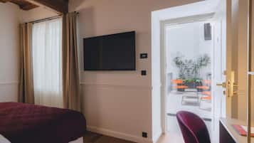 Une chambre d’hôtel avec un lit, un téléviseur fixé au mur et une porte donnant sur un balcon équipé de chaises et de plantes.