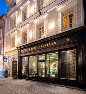 Un hôtel à la façade classique, doté de grandes fenêtres et d’une enseigne indiquant « HÔTEL HERITAGE ».