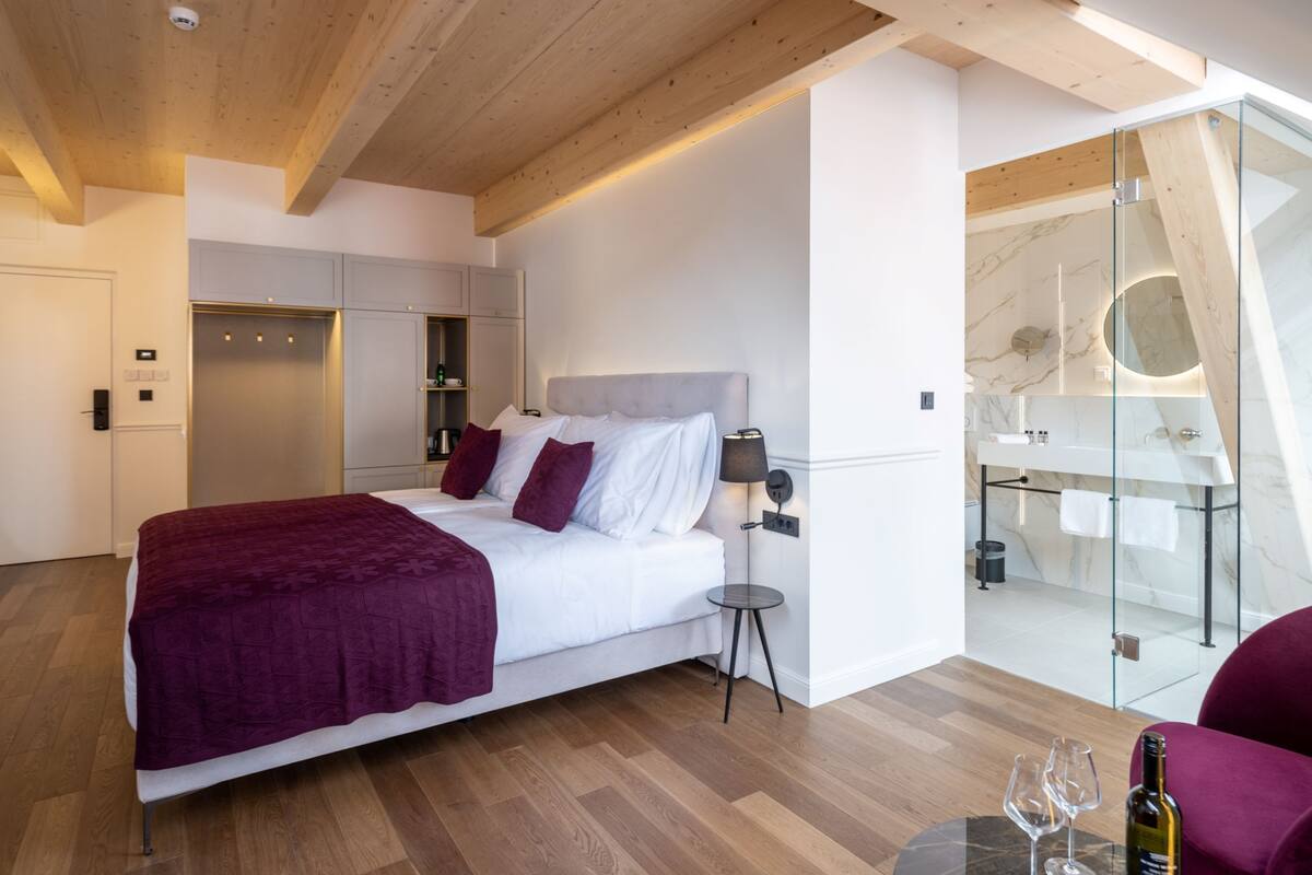 A modern hotel room with a large bed, a glass shower enclosure, and a wooden ceiling.