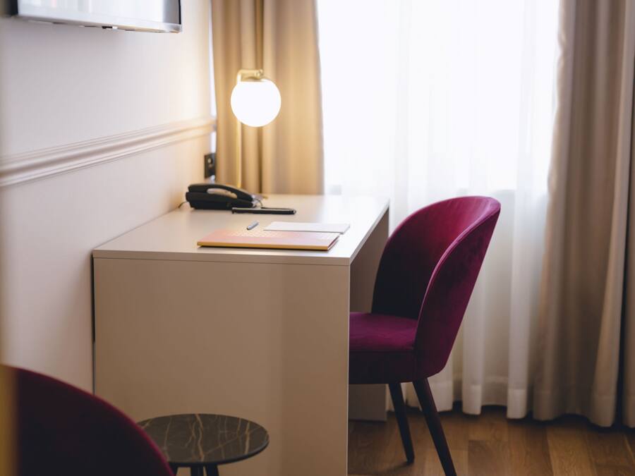 A hotel room with a desk, a chair, a lamp, and a small table.
