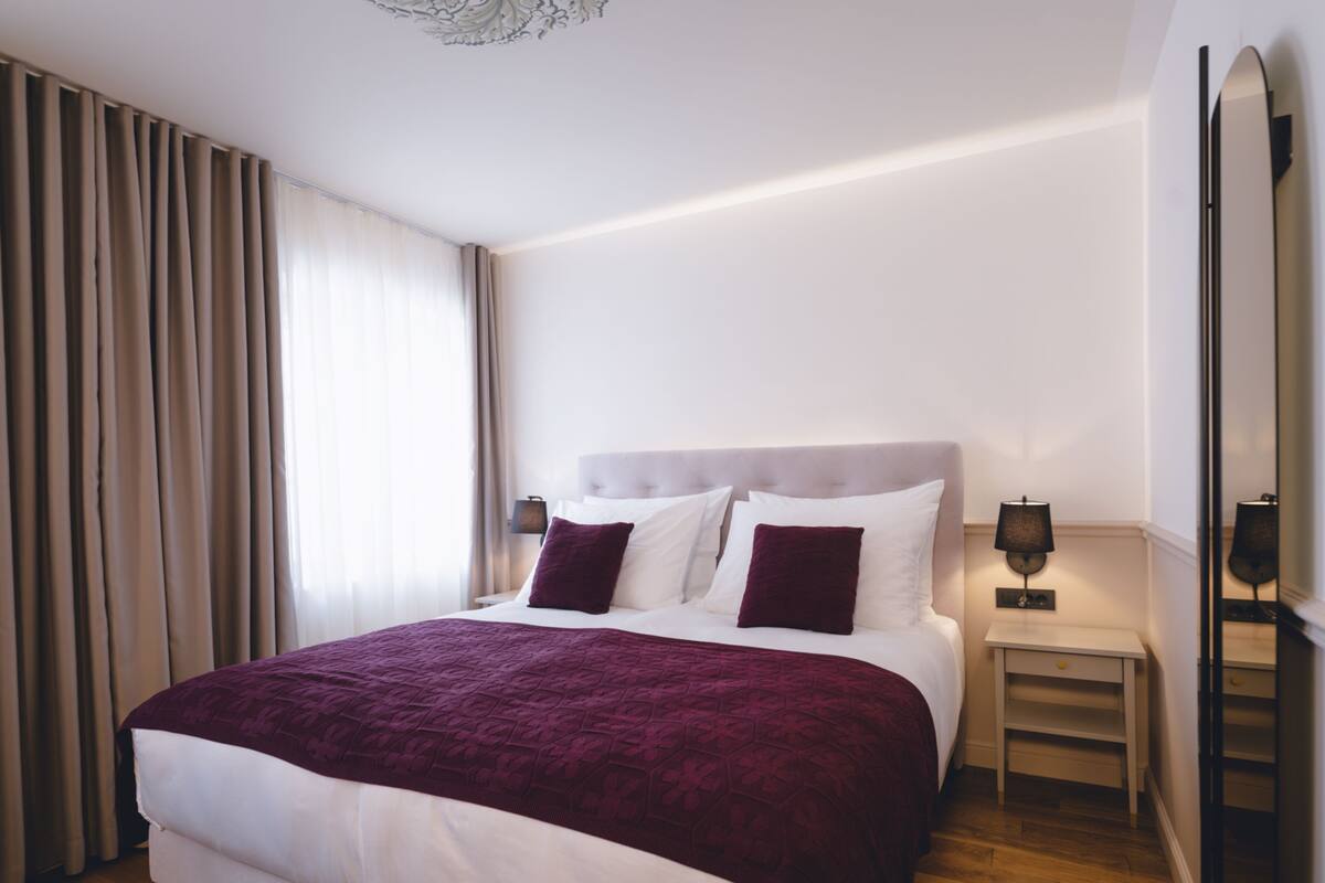 A modern hotel room with a large bed, a bedside table with a lamp, and a mirror on the wall.