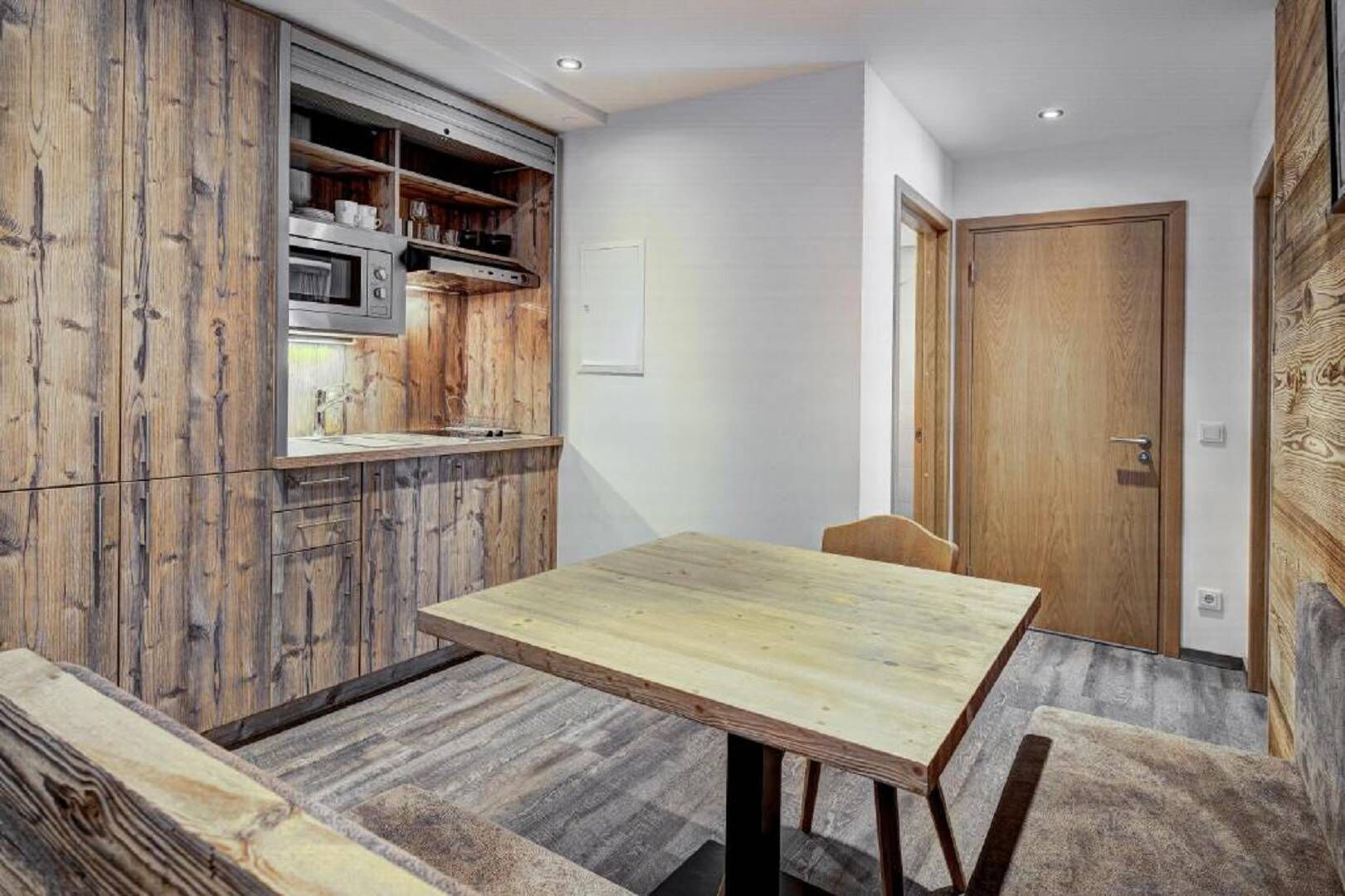 A compact kitchen with wooden cabinetry, a microwave, and a dining area with a table and chairs.