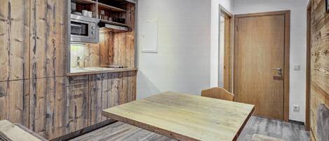 A compact kitchen with wooden cabinetry, a microwave, and a dining area with a table and chairs.