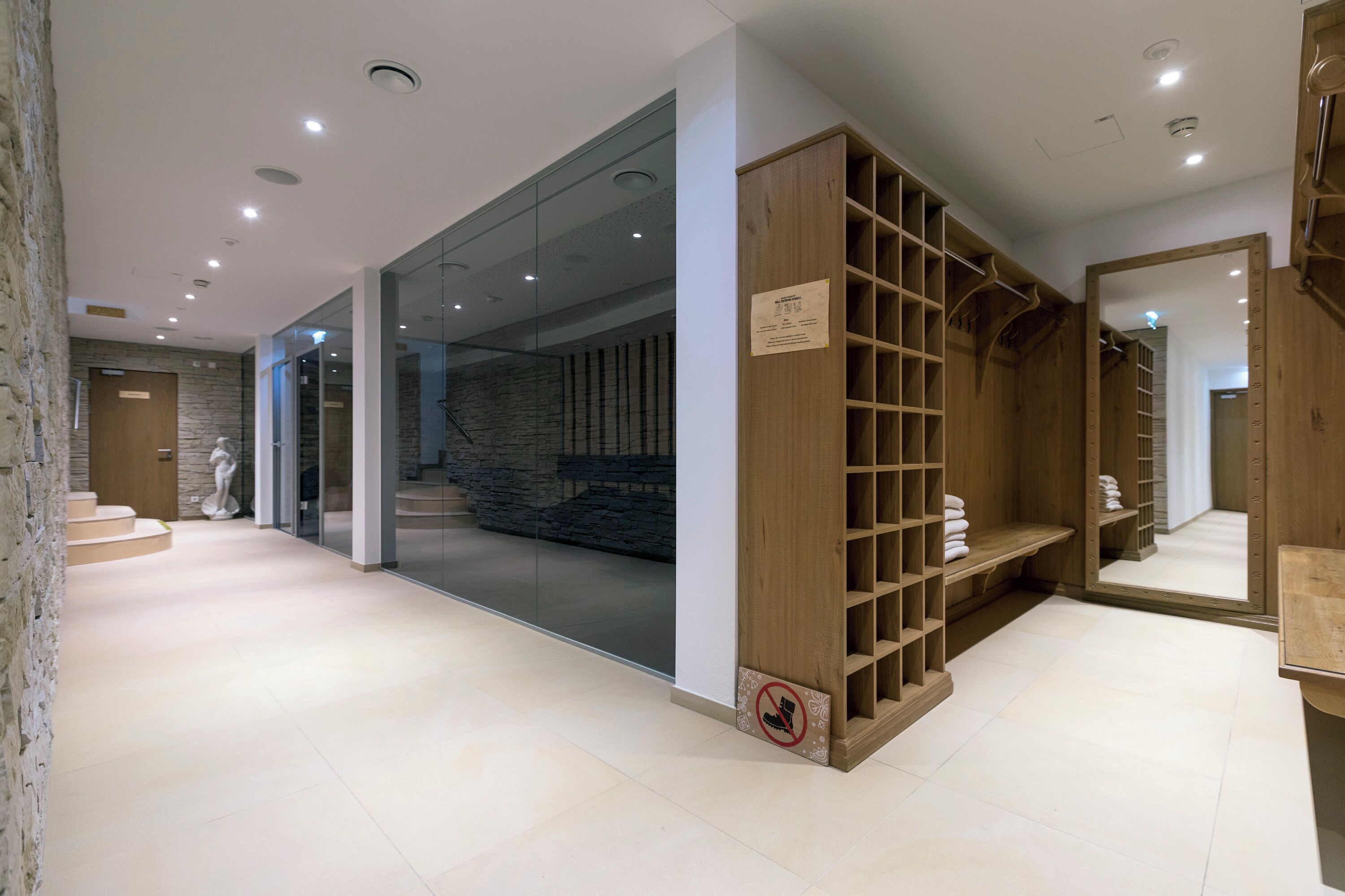 Una hall d'albergo moderna con una parete in pietra, un porta scarpe in legno e un grande specchio.