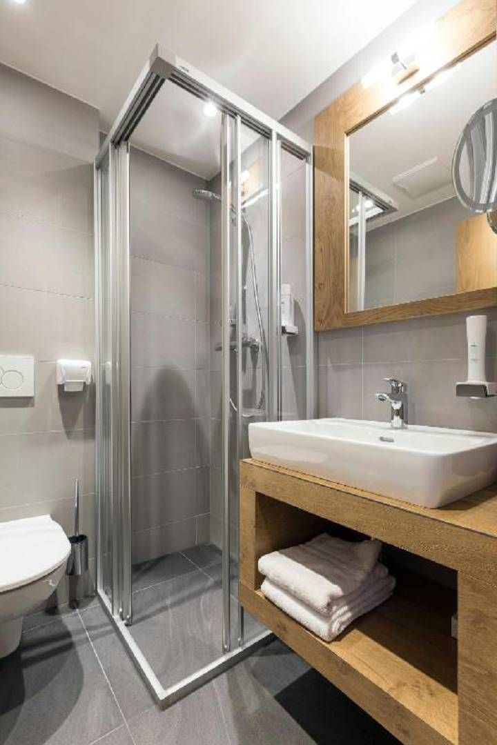 A modern bathroom with a glass-enclosed shower, a white sink, and a wooden vanity.
