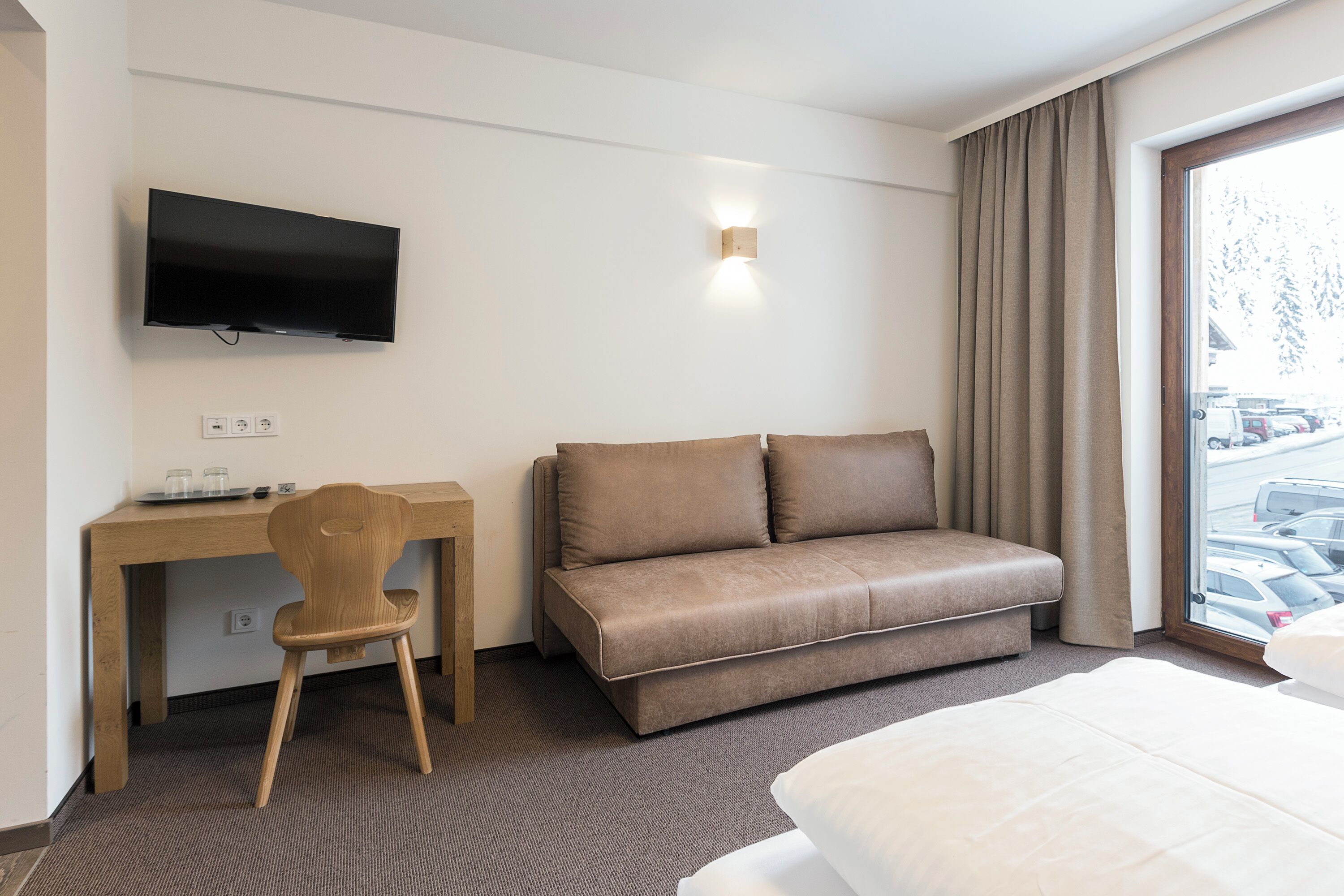 A hotel room with a bed, a sofa, a desk with a chair, a television, and a window with curtains.