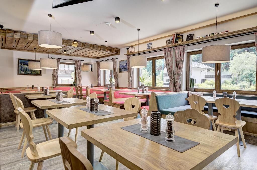A restaurant with wooden tables and chairs, a bar area, and large windows with curtains.