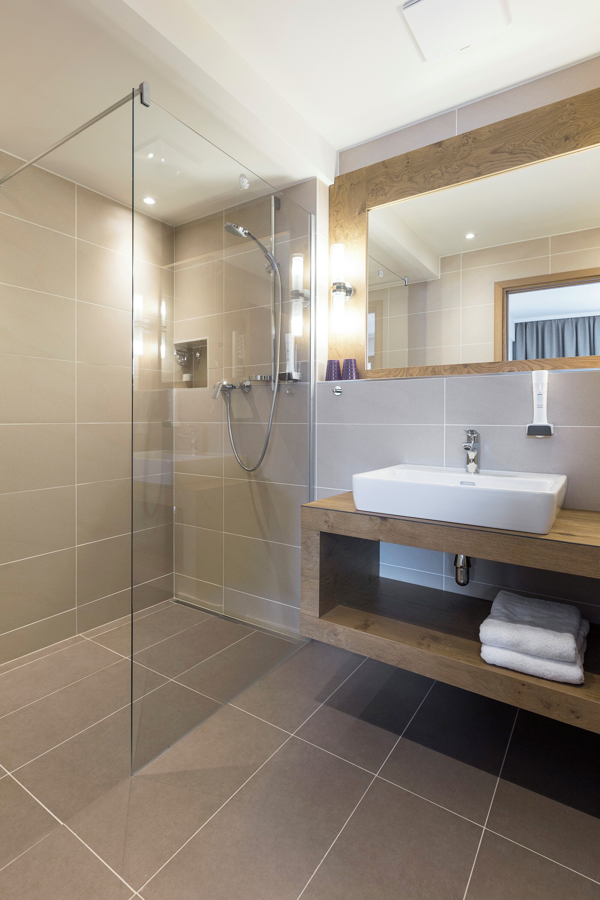 Un baño moderno con ducha de vidrio, lavamanos blanco y tocador de madera.