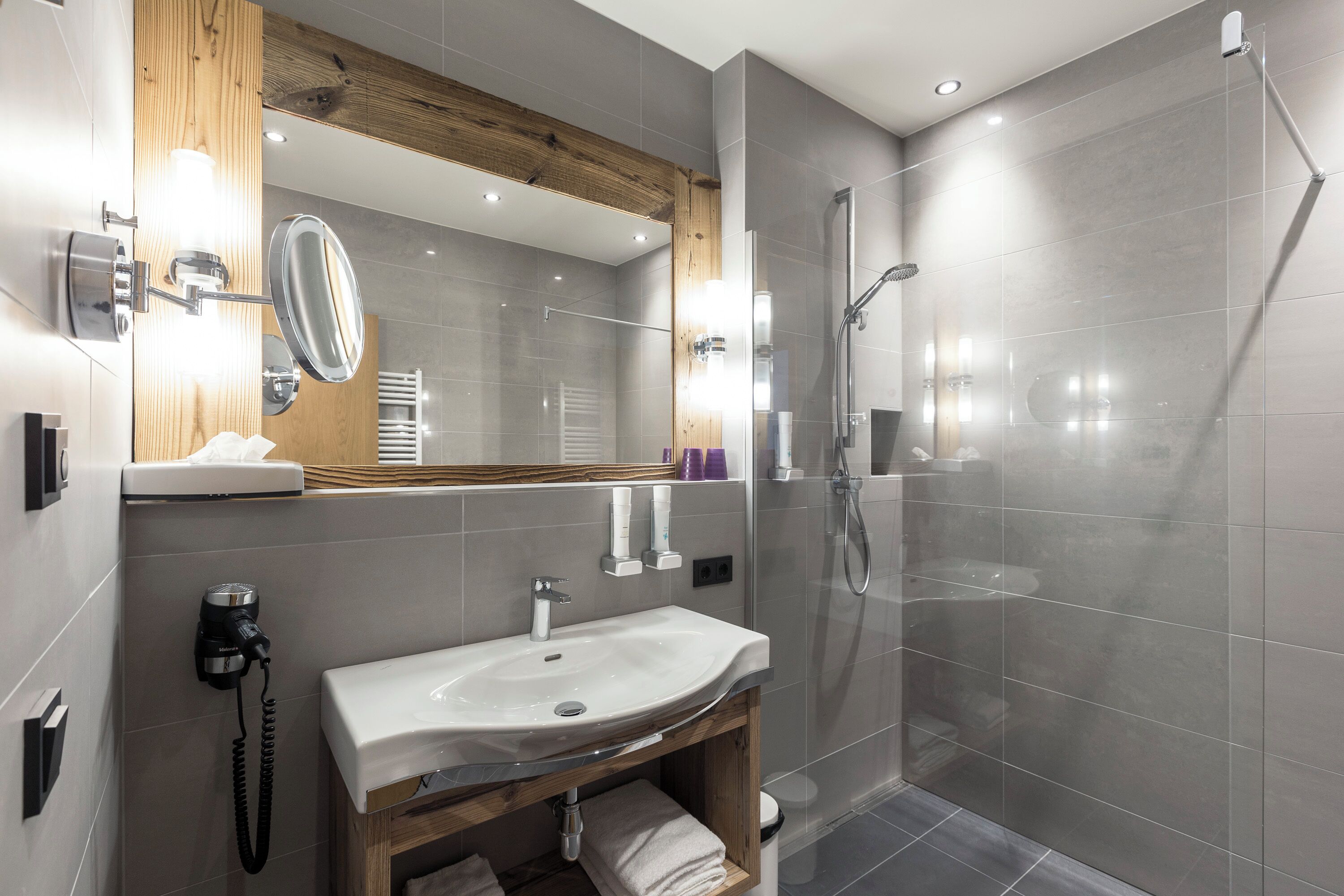 A modern bathroom with a glass-enclosed shower, a white sink, and a wooden vanity.