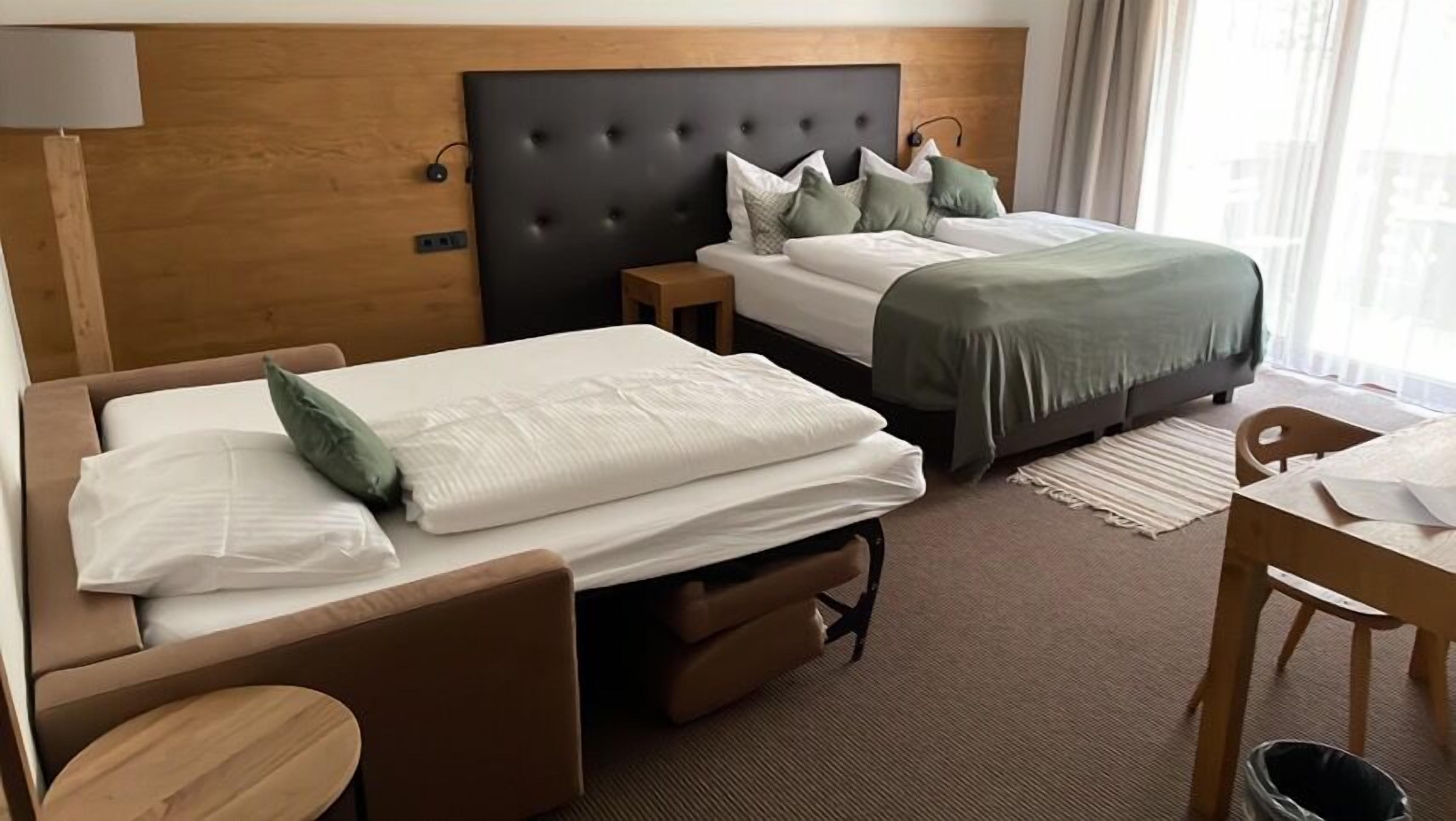 A hotel room with two beds, a wooden headboard, a small table, and a chair.