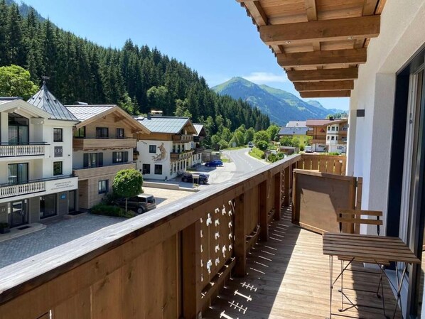 A wooden balcony with a view of a mountain and a village. - Das Glemm Hotel (Saalbach-Hinterglemm)