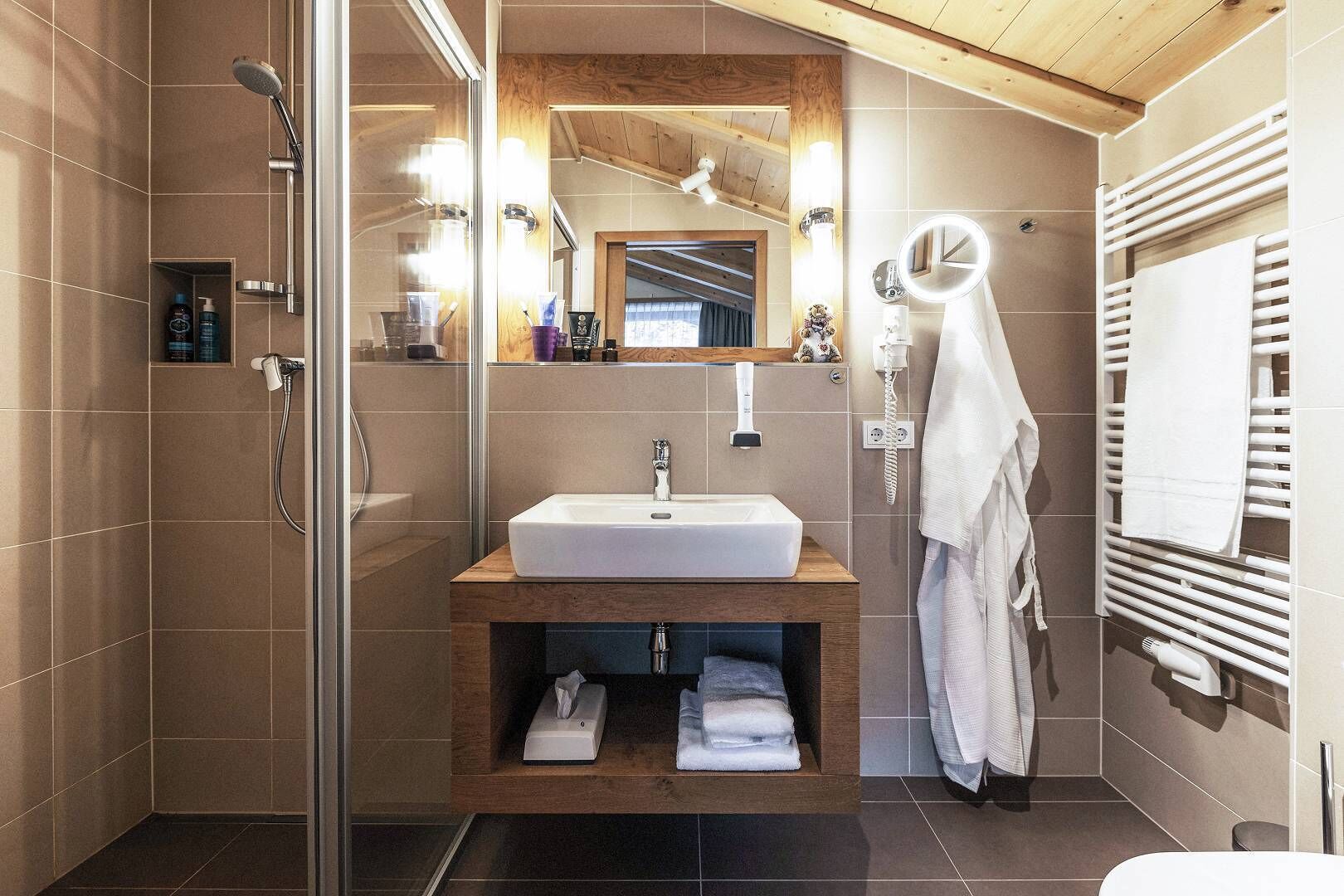 Un baño moderno con cabina de ducha de vidrio, tocador de madera con lavamanos y un perchero para toallas.