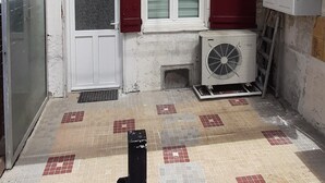 A courtyard with a tiled floor, a white door, red shutters, and a fan.