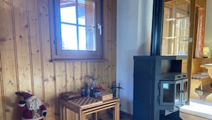 Una habitación acogedora con paredes de madera, una ventana, una chimenea, una pequeña mesa con un tablero de ajedrez y una figura de Papá Noel.