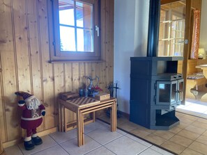 A cozy room with wooden walls, a window, a fireplace, a small table with a chessboard, and a Santa Claus figure.
