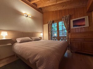 A room with a bed, two bedside lamps, a window with curtains, and a framed picture on the wall.