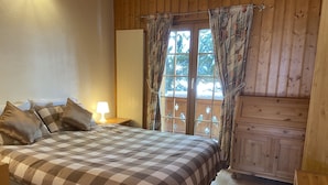 Un dormitorio con edredón a cuadros, una lámpara de noche y vistas a través de una ventana con cortinas.
