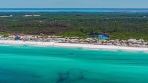 Eine Luftaufnahme einer Küstenlandschaft mit Strand, klarem türkisblauem Wasser und einem dichten Wald im Hintergrund.