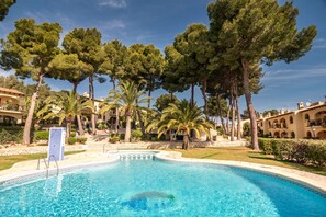 A swimming pool with a tiled border, surrounded by palm trees and a building with a tiled roof.
