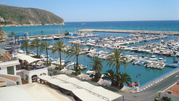 A marina with numerous boats docked, a rocky coastline, and a clear blue sky. - Casa Alta Apartment, Moraira, with 2 large community pools (Moraira)