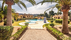 A pool area with a curved design, surrounded by palm trees and well-maintained hedges. - Casa Alta Apartment, Moraira, with 2 large community pools (Moraira)